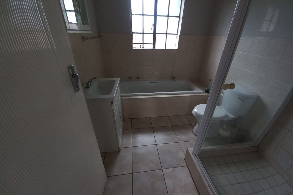 A functional bathroom featuring a built-in bathtub, a separate shower enclosure, a vanity basin, and a toilet with neutral floor and wall tiling.