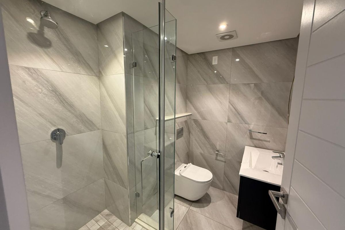 Modern bathroom featuring a glass-enclosed walk-in shower, wall-mounted toilet, and a sleek vanity unit with contemporary grey marble-look tiling throughout.