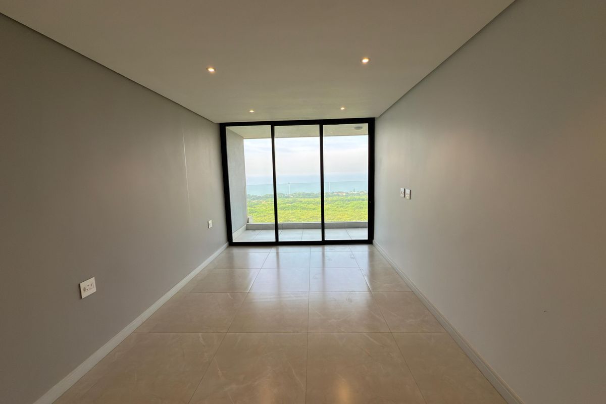 A bright, empty living area featuring large sliding glass doors that open to a balcony with scenic coastal views.