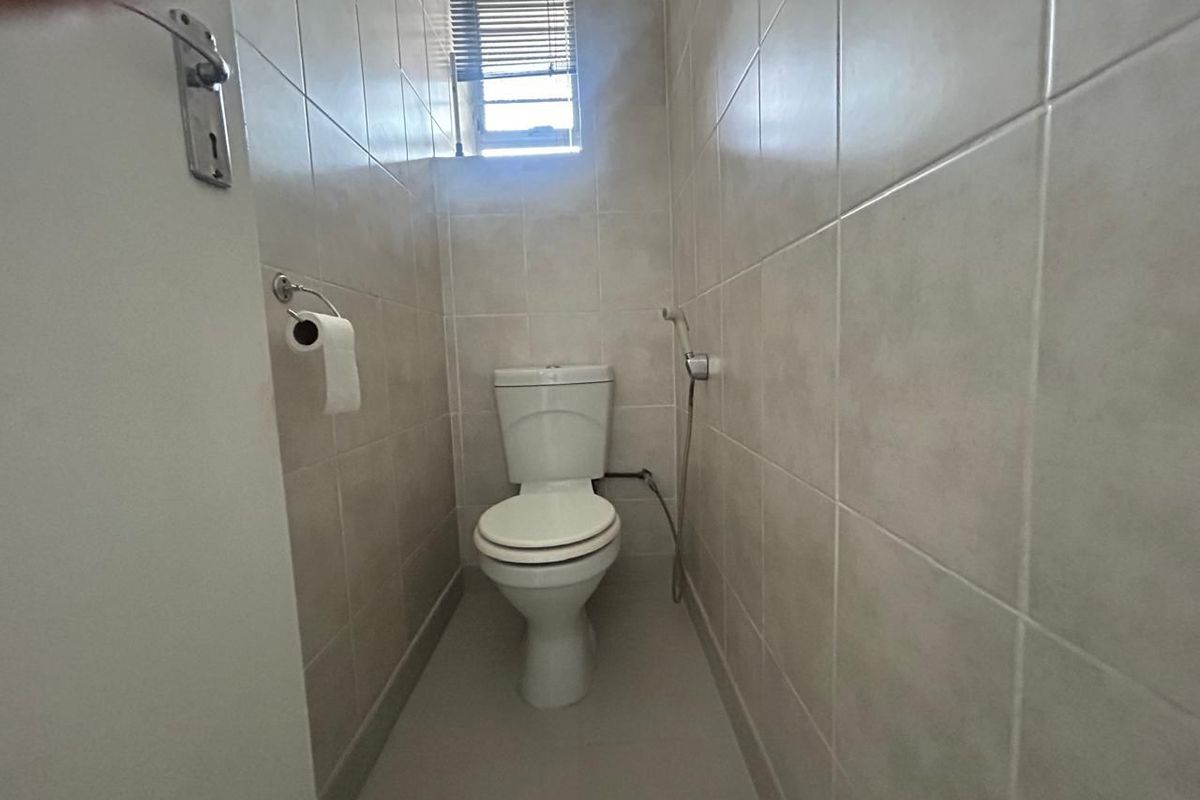 A compact bathroom featuring floor-to-ceiling wall tiles, a standard toilet, and a small window with fitted blinds.