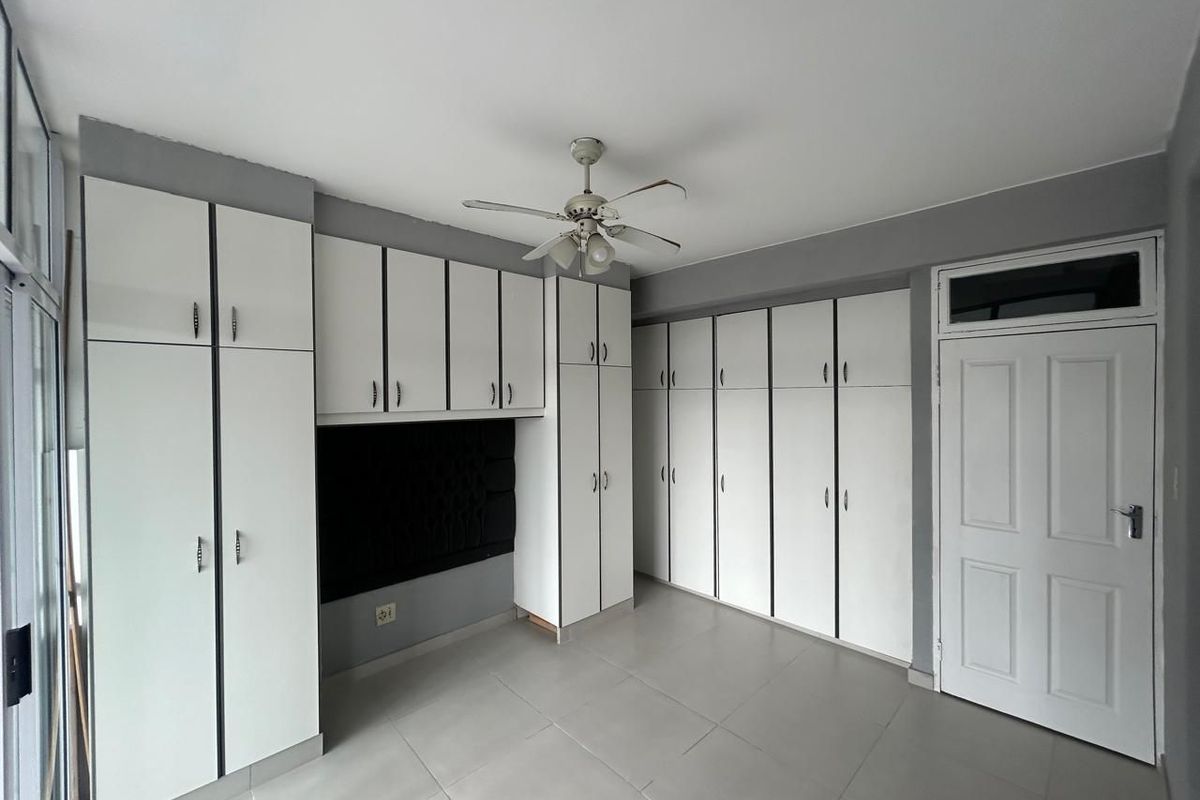 A bedroom featuring extensive built-in white cabinetry, tiled flooring, and a ceiling fan, offering ample storage space.