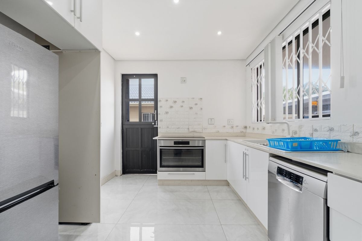 A clean, modern kitchen featuring white cabinetry, tiled flooring, a built-in oven, and a stable-style exterior door.
