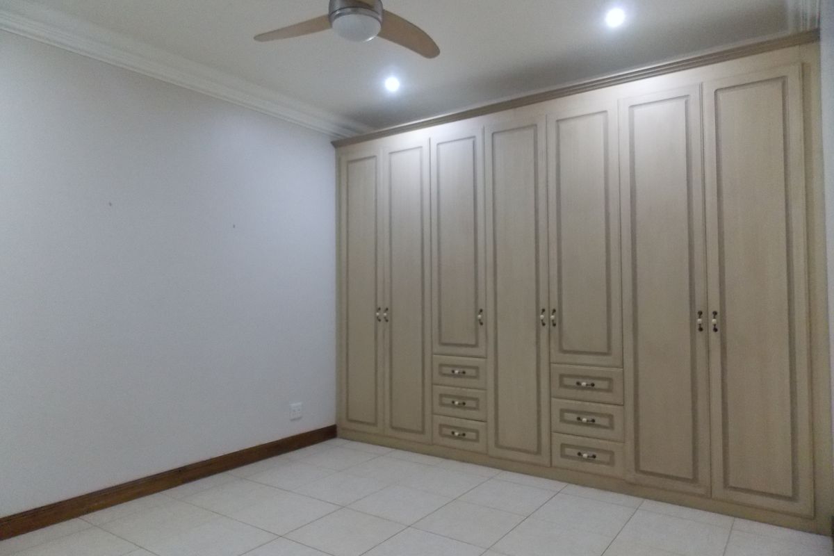 A spacious bedroom featuring extensive built-in cabinetry with integrated drawers, tiled flooring, and a ceiling fan.