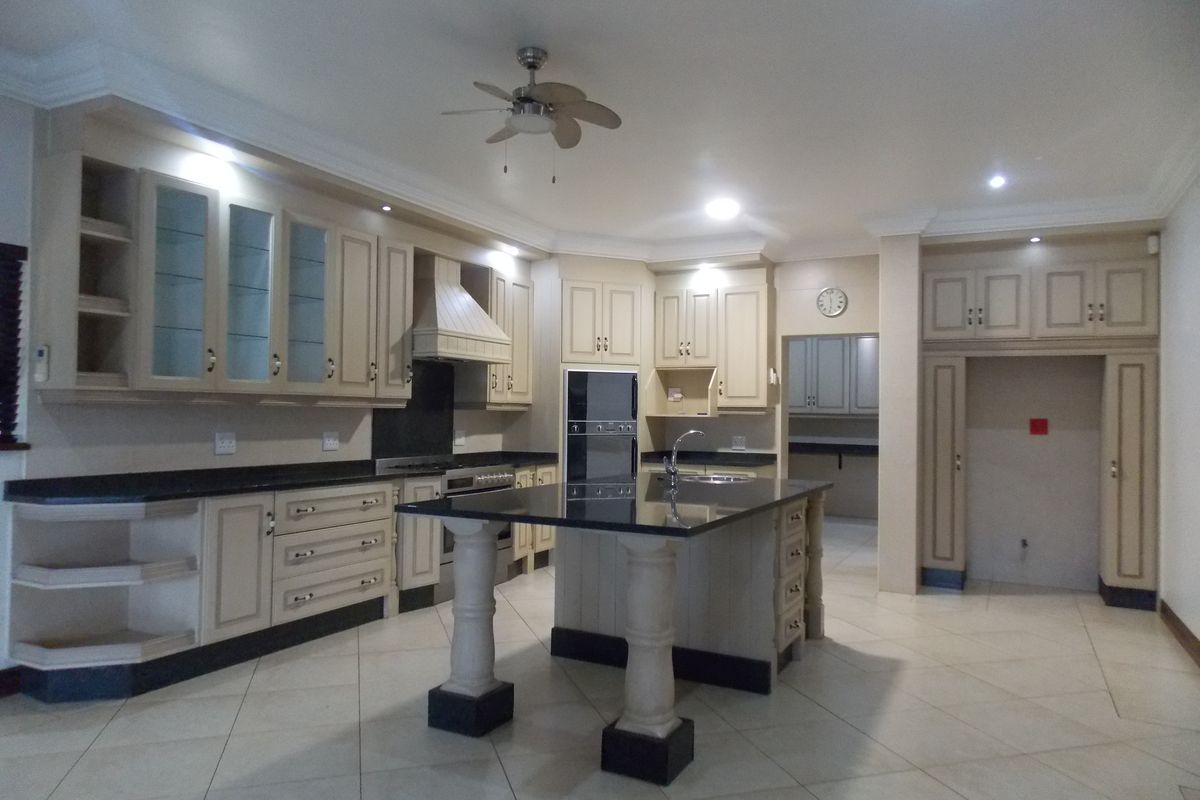 Spacious kitchen featuring cream cabinetry, black granite countertops, a central island with a sink, and integrated oven and extractor fan.