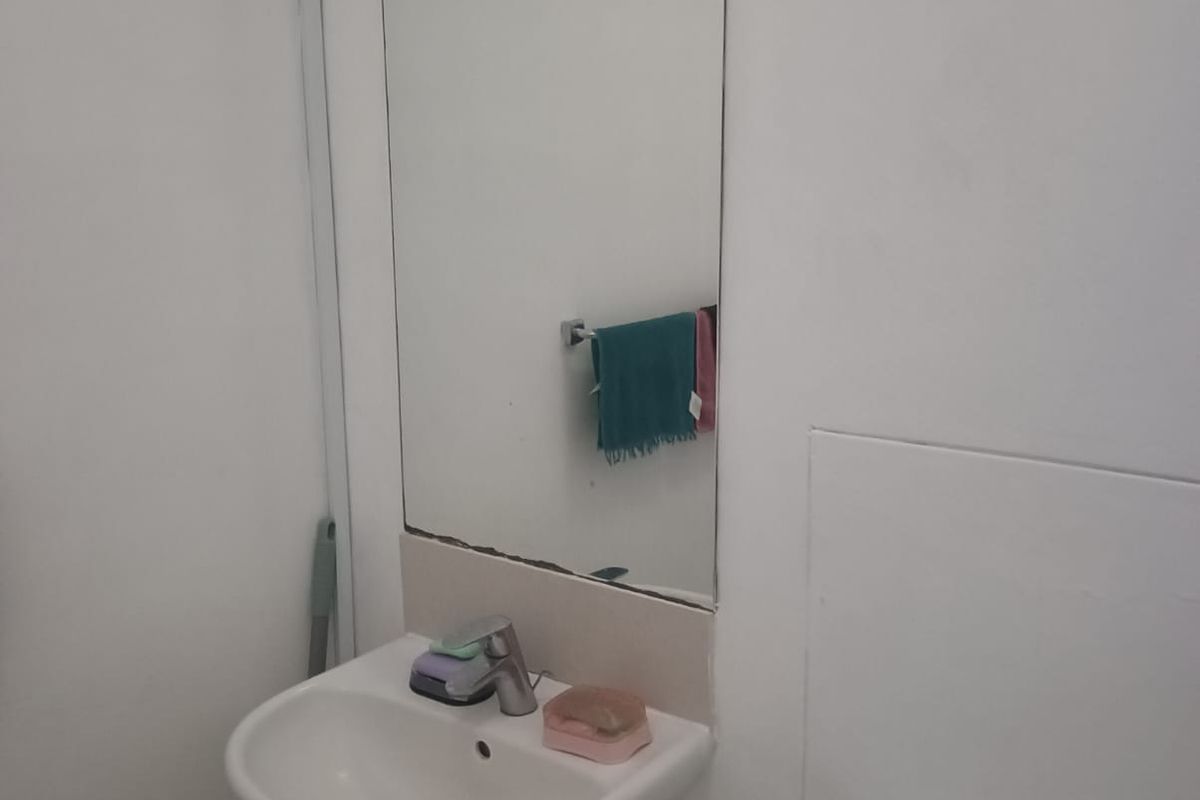 A compact bathroom featuring a wall-mounted basin, a toilet, and a large wall mirror.