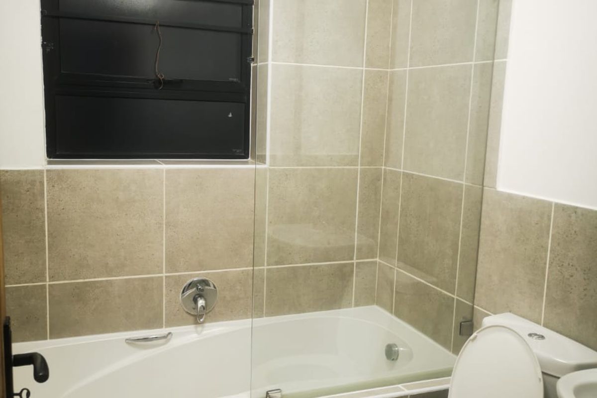 A functional bathroom featuring a built-in bathtub with a glass shower screen, wall-mounted shower head, and a standard toilet.