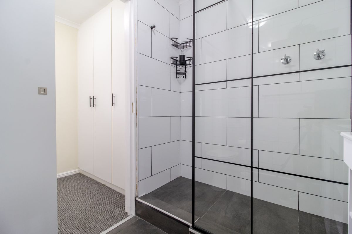 Modern bathroom featuring a walk-in shower with black-framed glass screen, subway-style wall tiles, and adjacent built-in storage cabinetry.