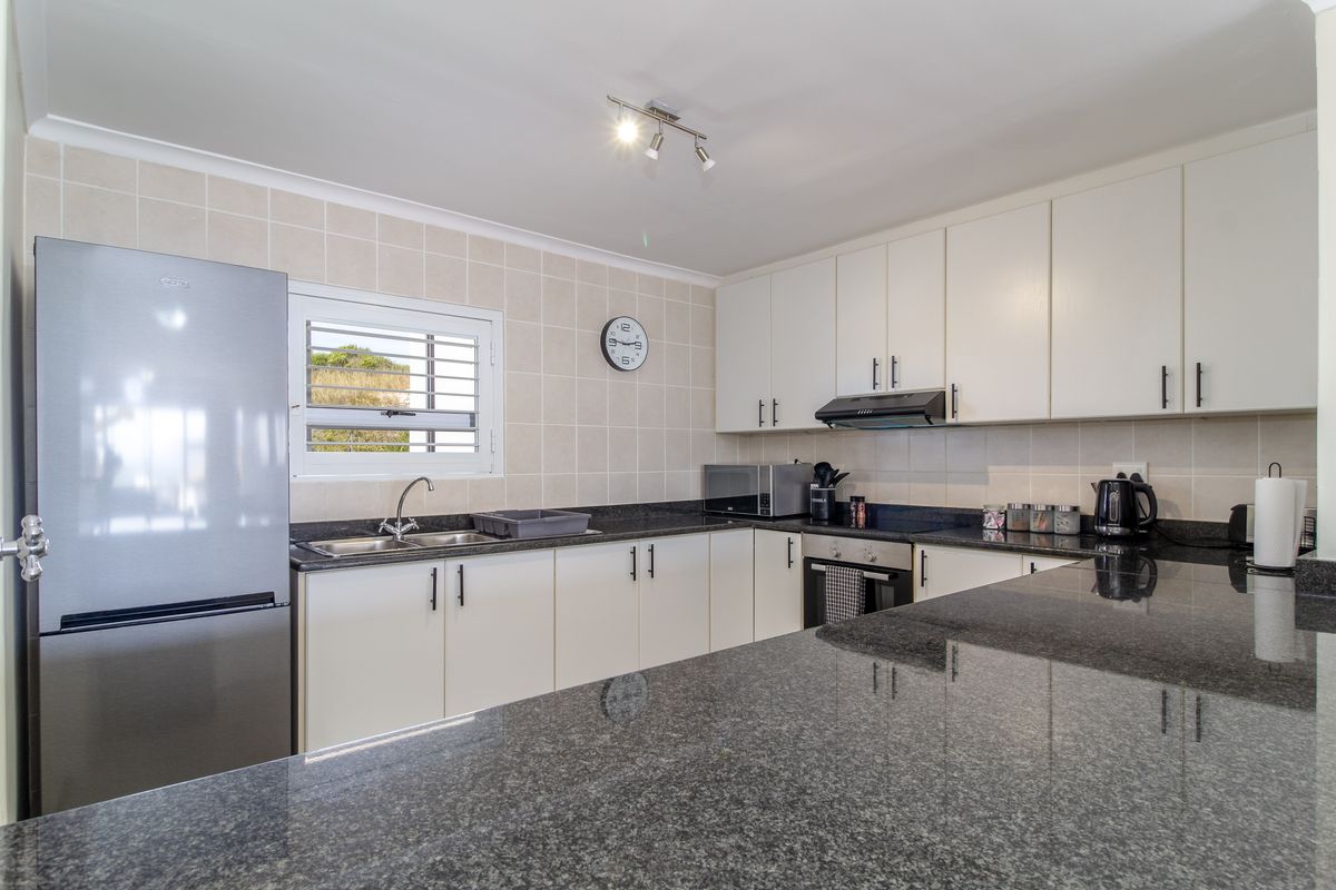 A functional kitchen featuring granite countertops, white cabinetry, a built-in oven, extractor fan, and a double sink with a window view.