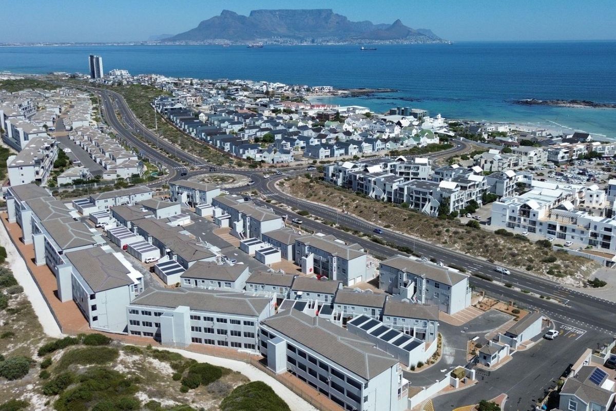 Aerial view of the apartment complex, showcasing the surrounding coastal neighborhood, road infrastructure, and proximity to the ocean and Table Mountain.