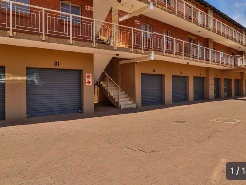 Exterior view of an apartment complex featuring multiple ground-level roller shutter garages and an external staircase leading to upper-level walkways.
