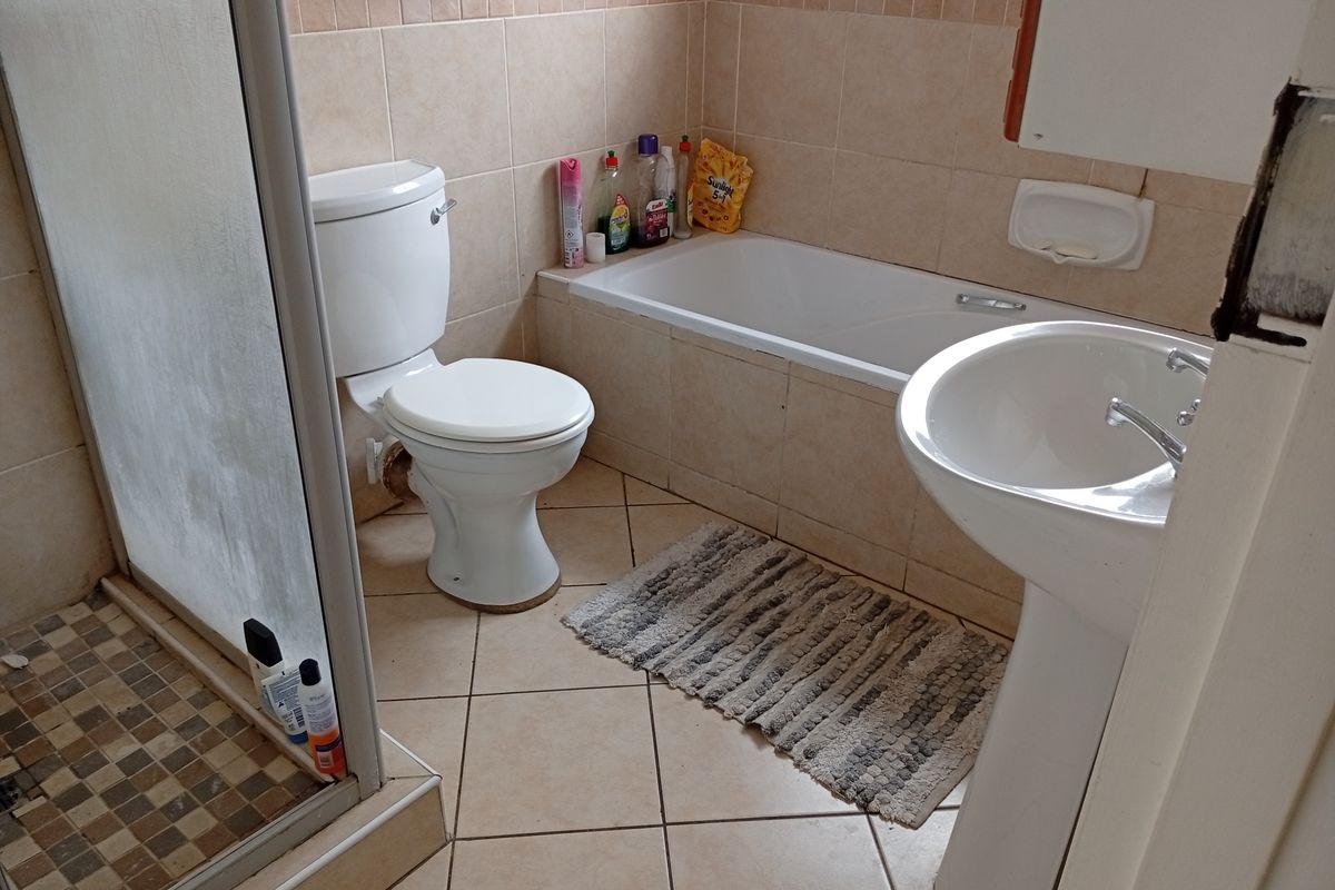 A functional bathroom featuring a shower enclosure, bathtub, pedestal basin, and neutral wall and floor tiling.