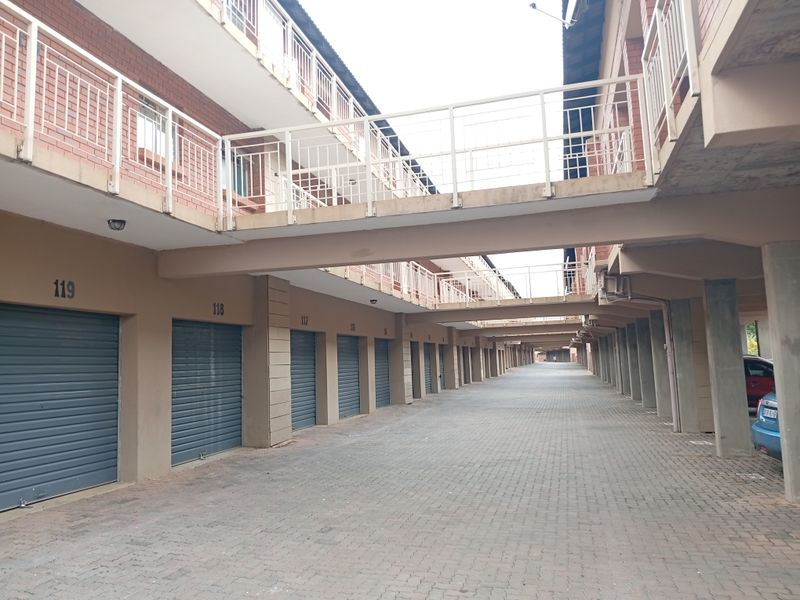 A view of a covered parking area featuring multiple individual roller shutter garage doors and elevated walkways connecting the apartment blocks.