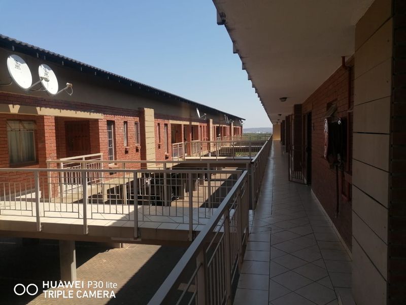 An exterior walkway or corridor in an apartment complex featuring tiled flooring, brick walls, and metal safety railings.
