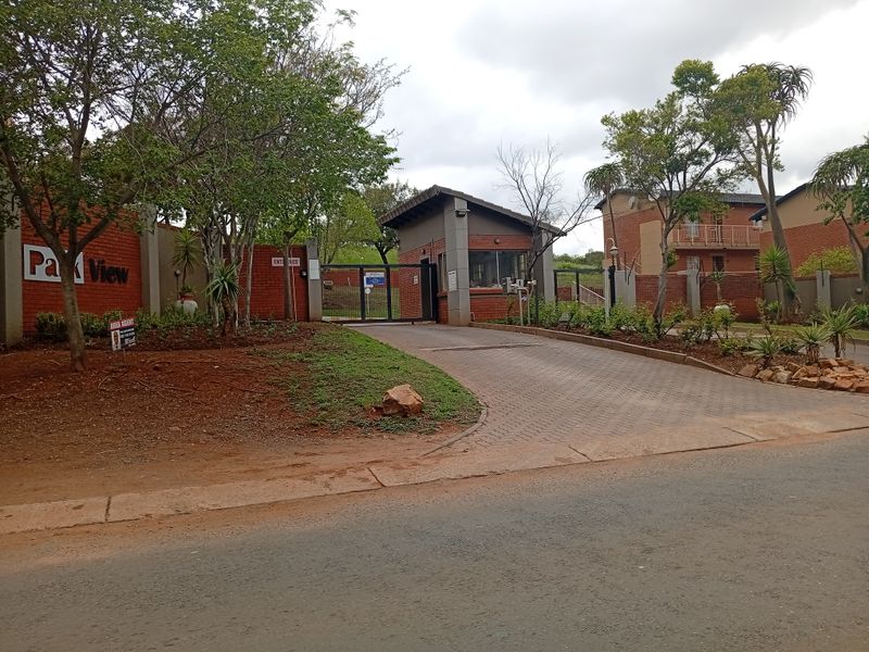 The entrance to Park View complex featuring a secure guard house, brick boundary walls, and a paved driveway access point.