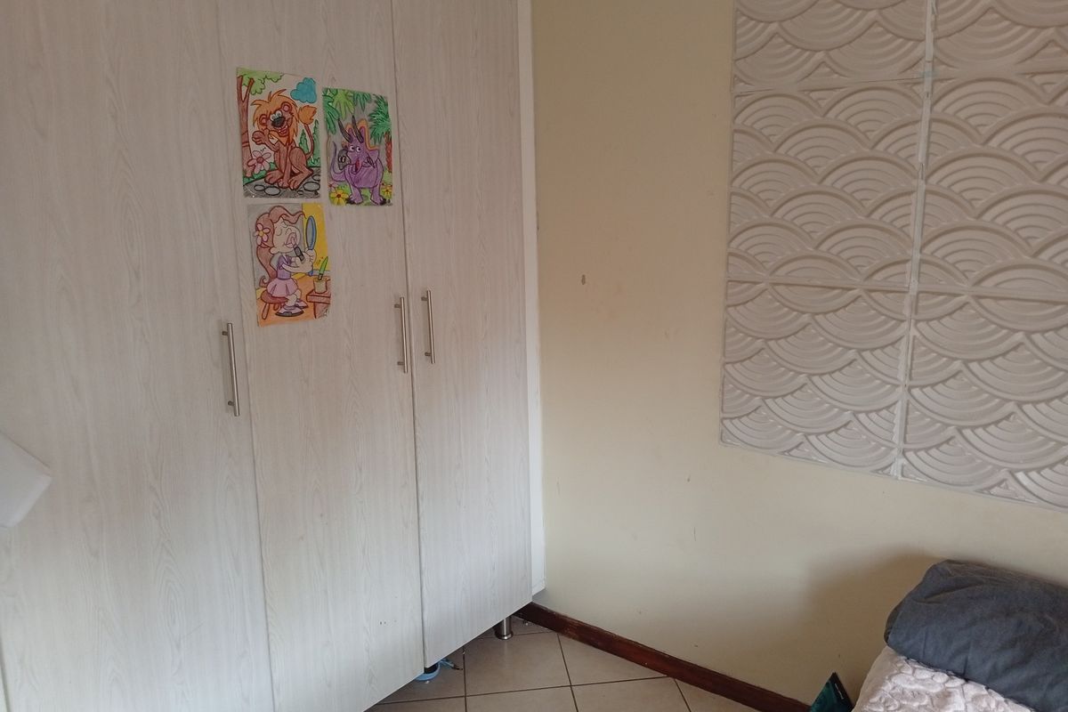 A bedroom featuring built-in wardrobes, tiled flooring, and decorative wall paneling, offering a functional space with potential for cosmetic updates.