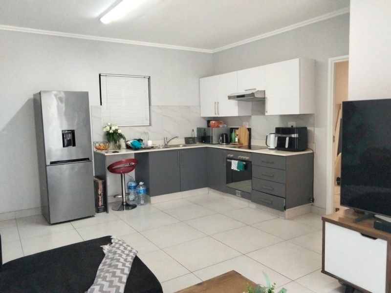Modern open-plan kitchen featuring grey base cabinetry, white wall units, tiled backsplash, and integrated oven with extractor fan.