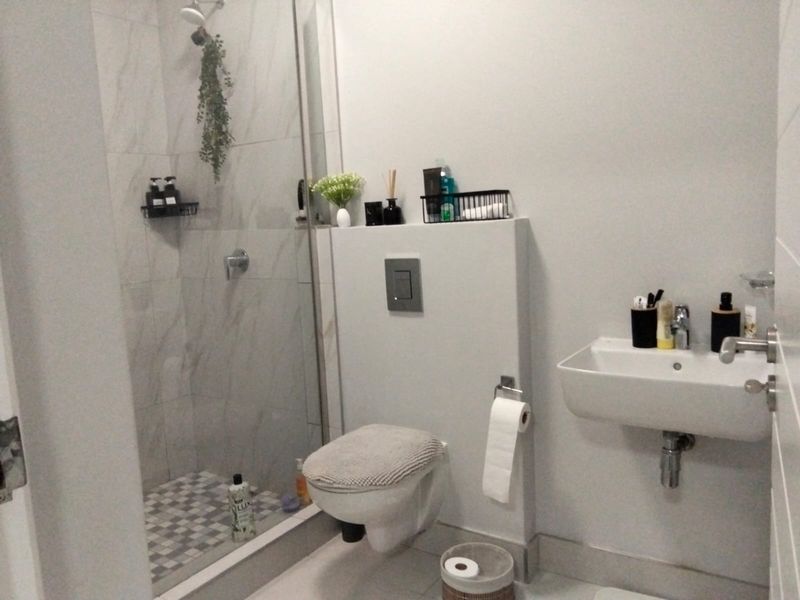 Modern bathroom featuring a wall-mounted toilet, a floating vanity sink, and a walk-in shower with marble-look wall tiles and mosaic floor tiling.