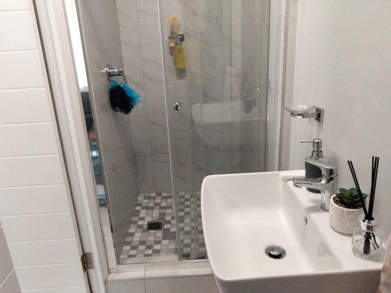 A modern bathroom featuring a glass-enclosed shower with mosaic floor tiling and a contemporary wall-mounted basin with chrome fixtures.