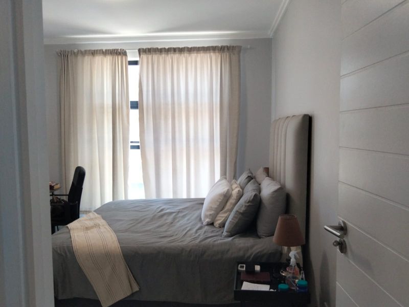 A well-lit bedroom featuring neutral wall tones, a modern horizontal-panel interior door, and large window with floor-to-ceiling curtains.