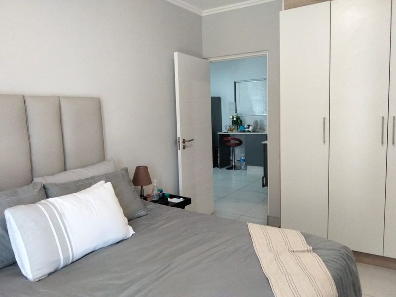 A well-maintained bedroom featuring built-in wardrobes and neutral finishes, with a view through the doorway into an adjacent kitchen area.