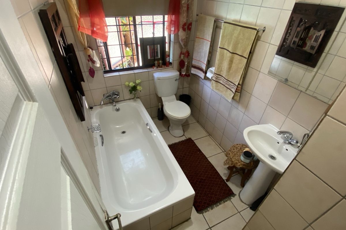 A compact bathroom featuring a standard bathtub, pedestal basin, and toilet with full-height wall tiling and a security-grilled window.