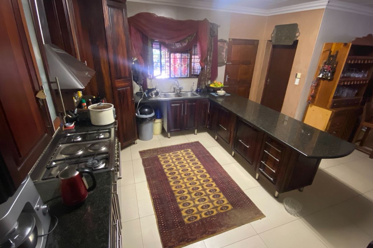A functional kitchen featuring dark wood cabinetry, granite countertops, a gas hob, and an integrated breakfast bar area.