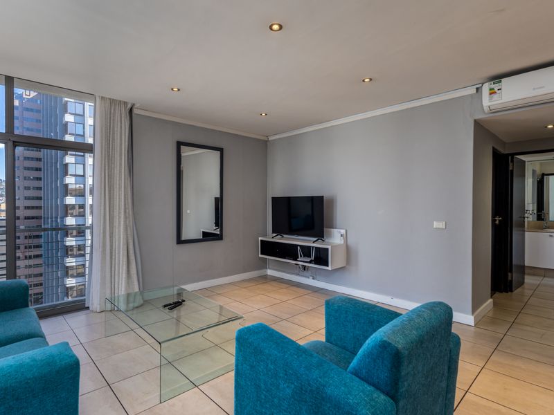 A bright living room featuring tiled floors, recessed lighting, a wall-mounted air conditioning unit, and access to a balcony with city views.