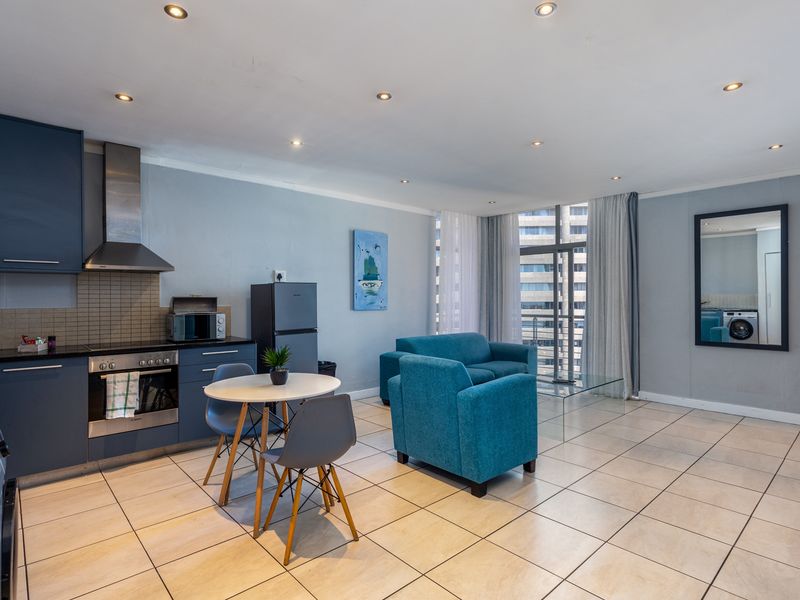 Open-plan living area featuring a modern kitchen with dark cabinetry, stainless steel appliances, tiled flooring, and access to a balcony through sliding glass doors.