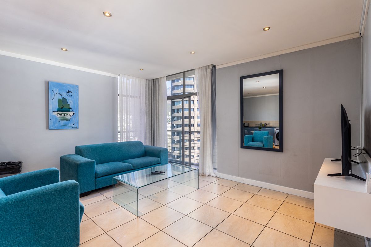 A bright and open living room featuring tiled flooring, recessed downlighting, and a large sliding glass door providing access to the balcony.