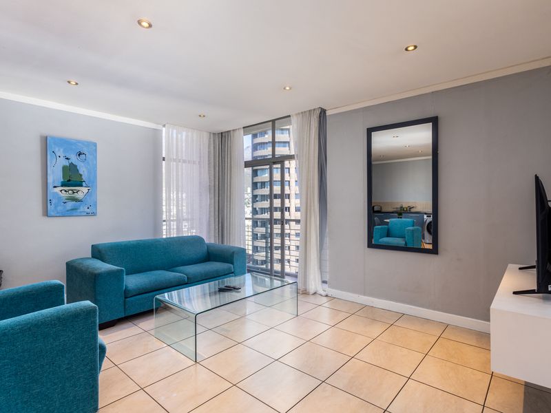 A bright and open living room featuring tiled flooring, recessed downlighting, and a large sliding glass door providing access to the balcony.