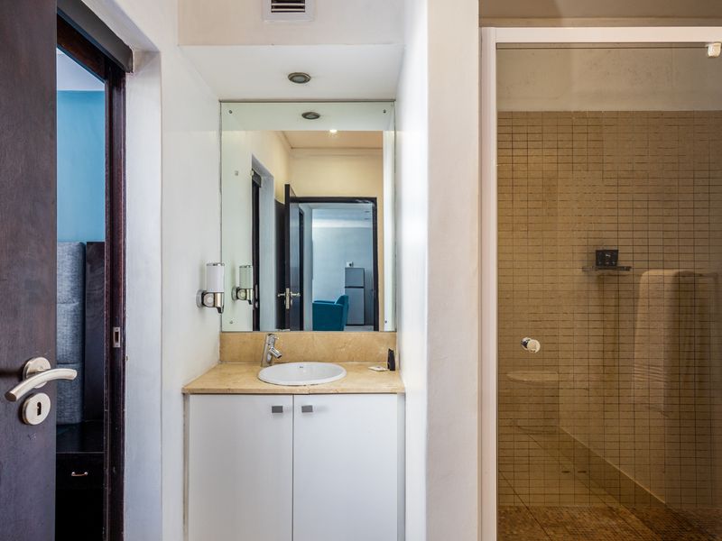 A functional bathroom featuring a vanity with stone countertop, integrated sink, wall mirror, and a separate shower enclosure with tiled walls.