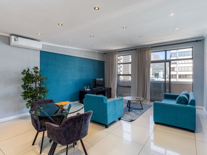 A bright, open-plan living area featuring tiled floors, recessed lighting, a wall-mounted air conditioner, and large sliding doors leading to a balcony with city views.