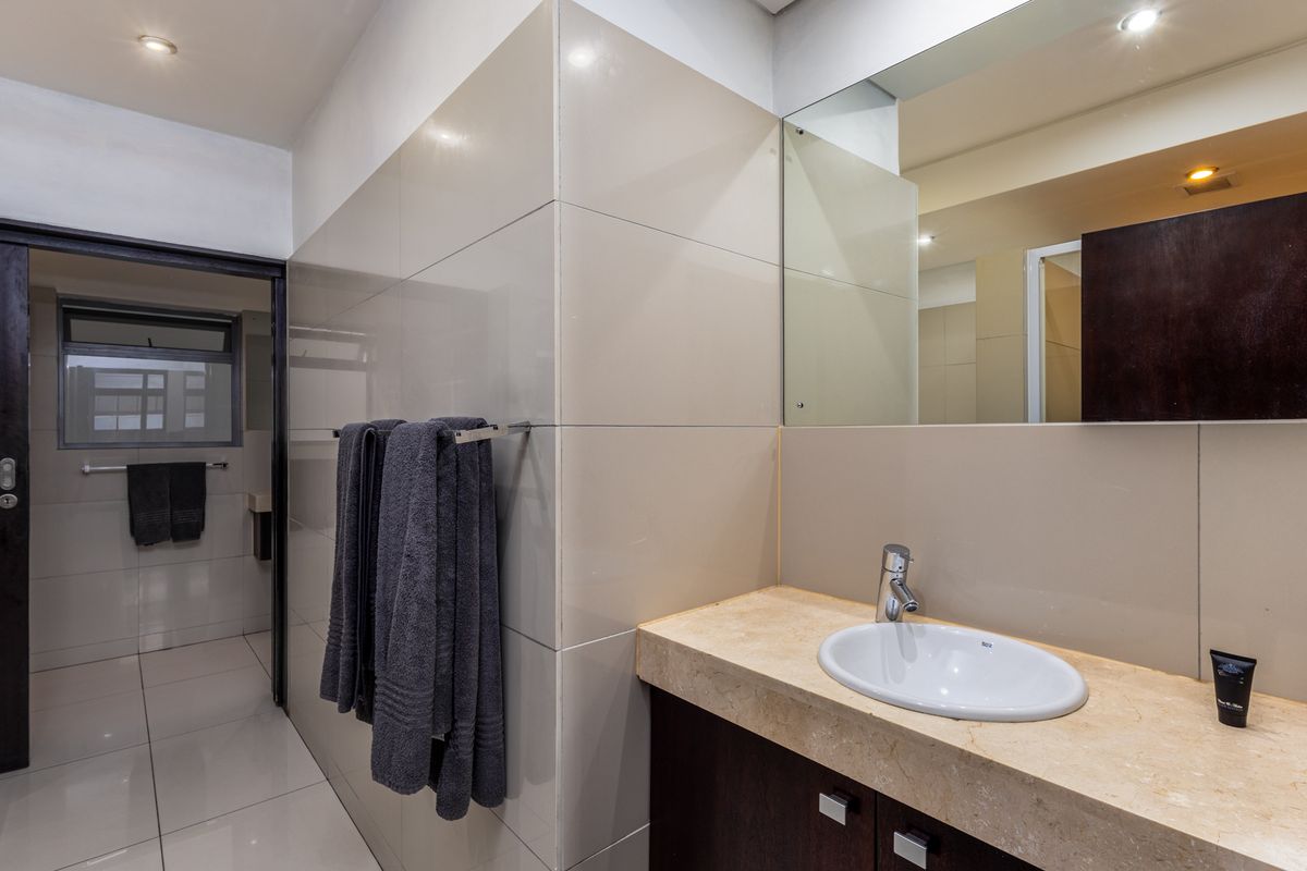 Modern bathroom featuring a stone-topped vanity with an integrated sink, large wall mirror, recessed lighting, and neutral wall tiling.