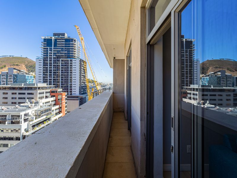 A narrow balcony with tiled flooring and a concrete balustrade, offering an elevated urban view of the surrounding city skyline.