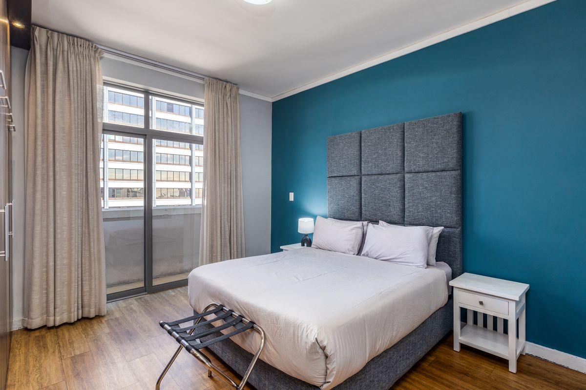 A well-maintained bedroom featuring laminate flooring, a built-in wardrobe, and a large sliding glass door providing natural light.