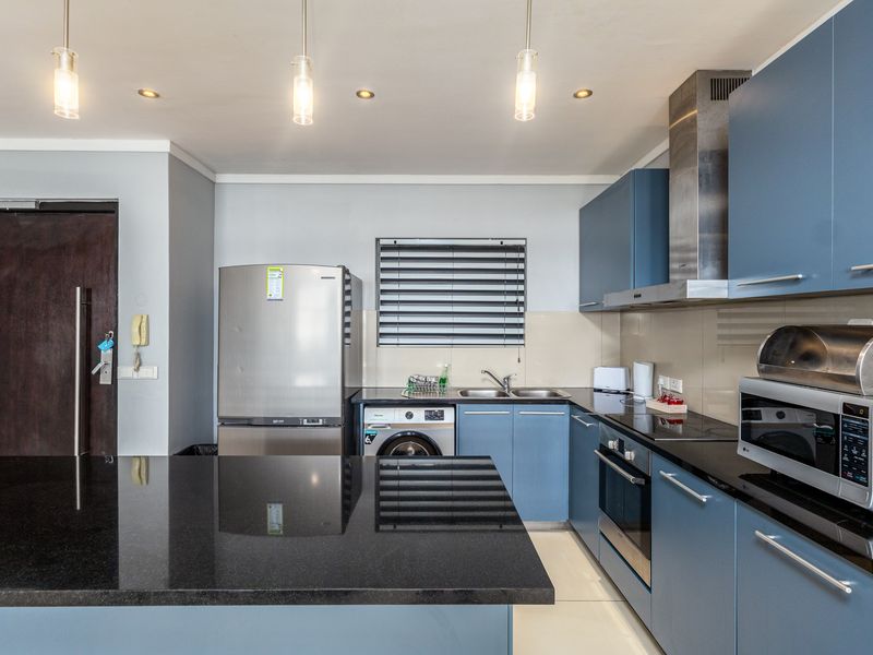 Modern kitchen featuring blue cabinetry, black granite countertops, integrated appliances, and a central island, providing a functional and stylish cooking space.