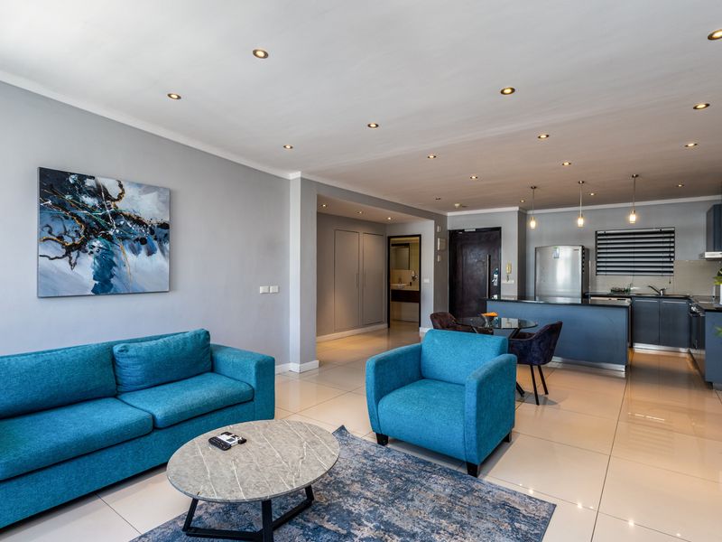 Modern open-plan living area featuring sleek kitchen cabinetry, stone countertops, recessed lighting, and polished porcelain floor tiles throughout the space.
