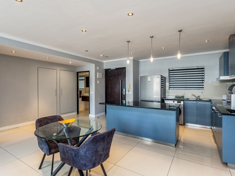 Modern open-plan kitchen and dining area featuring blue cabinetry, granite countertops, tiled flooring, and contemporary pendant lighting.