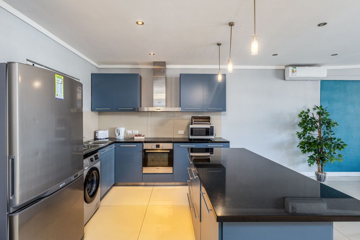 Modern kitchen featuring blue cabinetry, granite countertops, stainless steel appliances, integrated laundry, and a central island, complemented by recessed and pendant lighting.