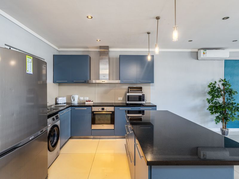 Modern kitchen featuring blue cabinetry, granite countertops, stainless steel appliances, integrated laundry, and a central island, complemented by recessed and pendant lighting.