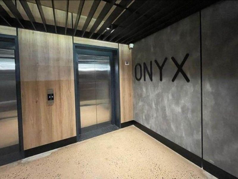 Modern apartment building elevator lobby featuring contemporary wood paneling, polished concrete-style walls, and sleek stainless steel elevator doors.