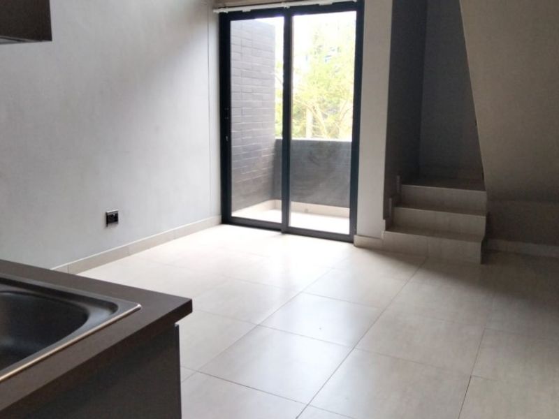 Open plan living area featuring tiled flooring, a built-in kitchen counter with sink, and sliding glass doors leading to a private balcony.