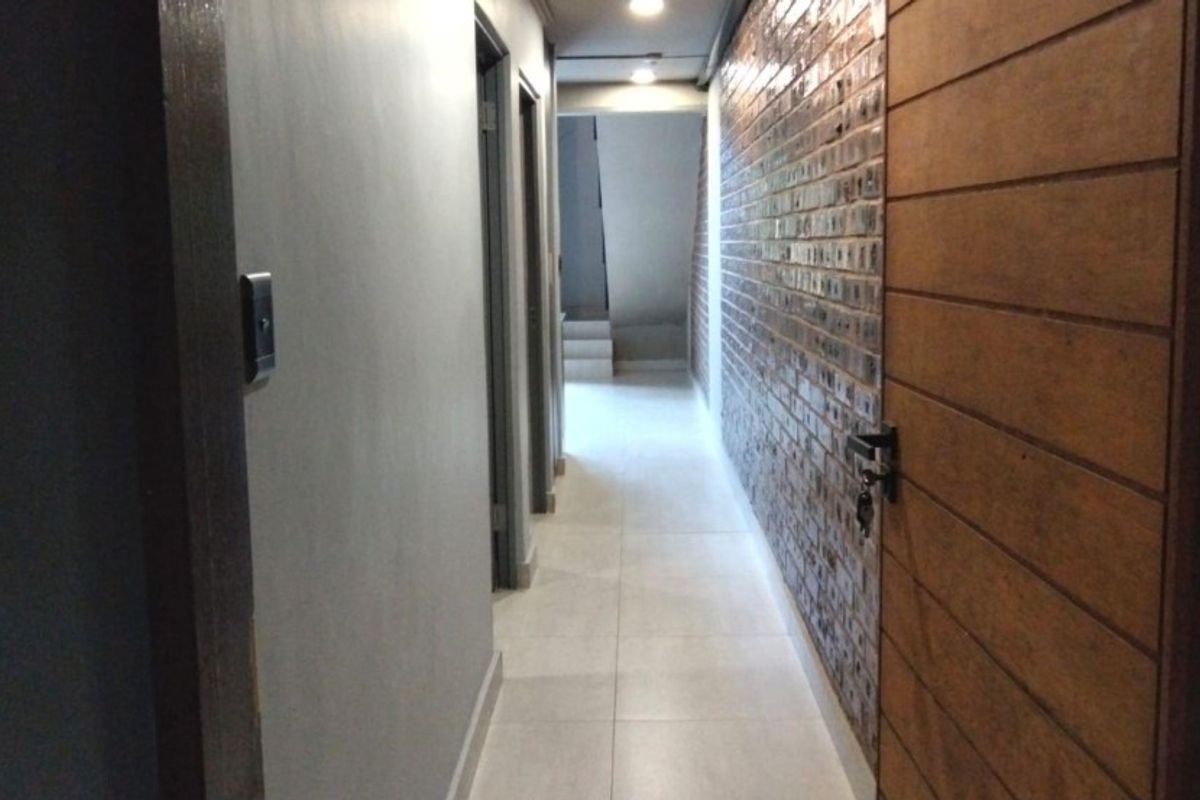 A well-lit interior hallway featuring tiled flooring, a decorative brick-style accent wall, and modern wooden door finishes.