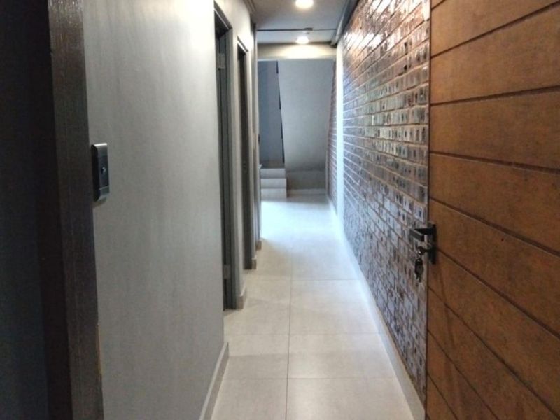 A well-lit interior hallway featuring tiled flooring, a decorative brick-style accent wall, and modern wooden door finishes.