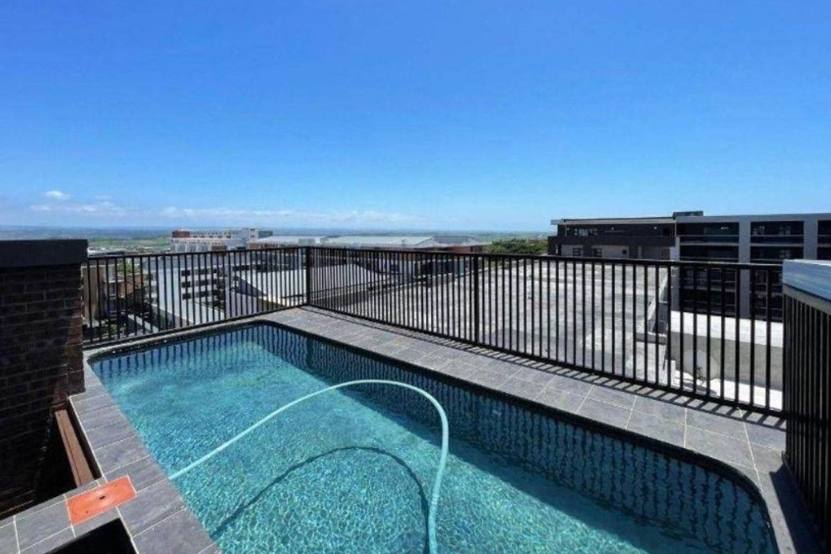 A rooftop swimming pool featuring tiled surround and metal safety railings, offering expansive elevated views of the surrounding urban landscape.