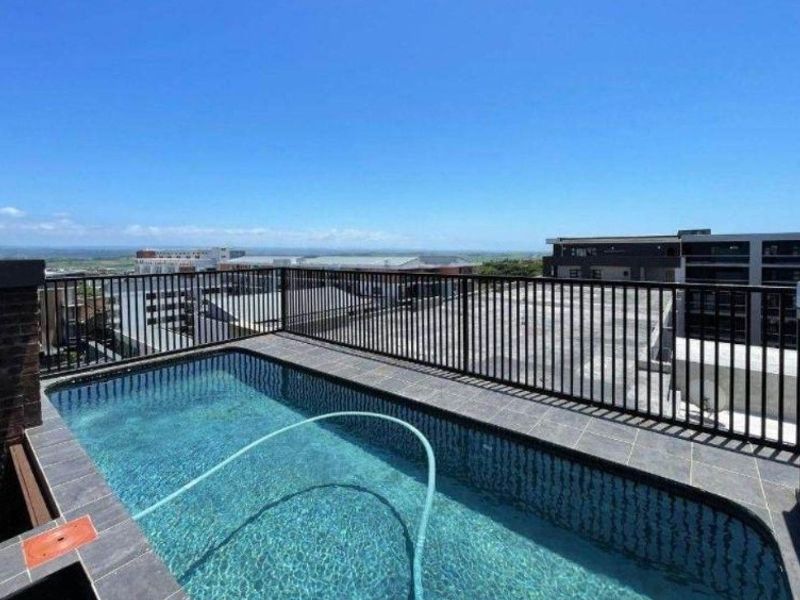A rooftop swimming pool featuring tiled surround and metal safety railings, offering expansive elevated views of the surrounding urban landscape.