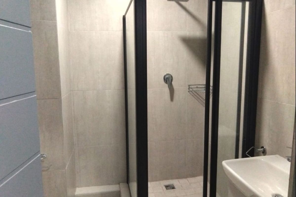 Modern bathroom featuring a walk-in shower with a black frame, rainfall showerhead, and a wall-mounted basin with neutral tiled finishes.