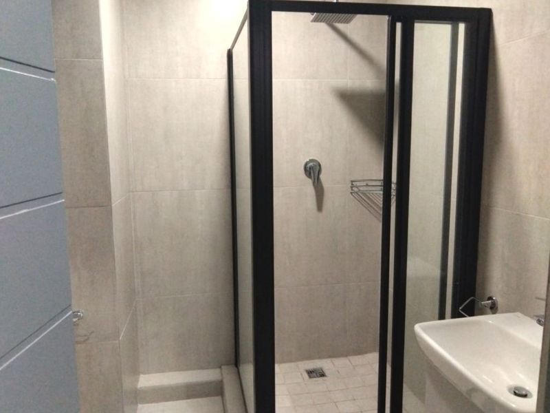 Modern bathroom featuring a walk-in shower with a black frame, rainfall showerhead, and a wall-mounted basin with neutral tiled finishes.