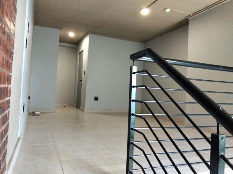 An open-plan interior space featuring tiled flooring, a modern metal staircase railing, and exposed brick wall accents.
