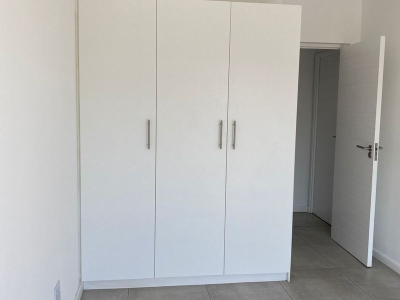 A clean bedroom featuring built-in white cabinetry, modern grey floor tiles, and a neutral interior finish.